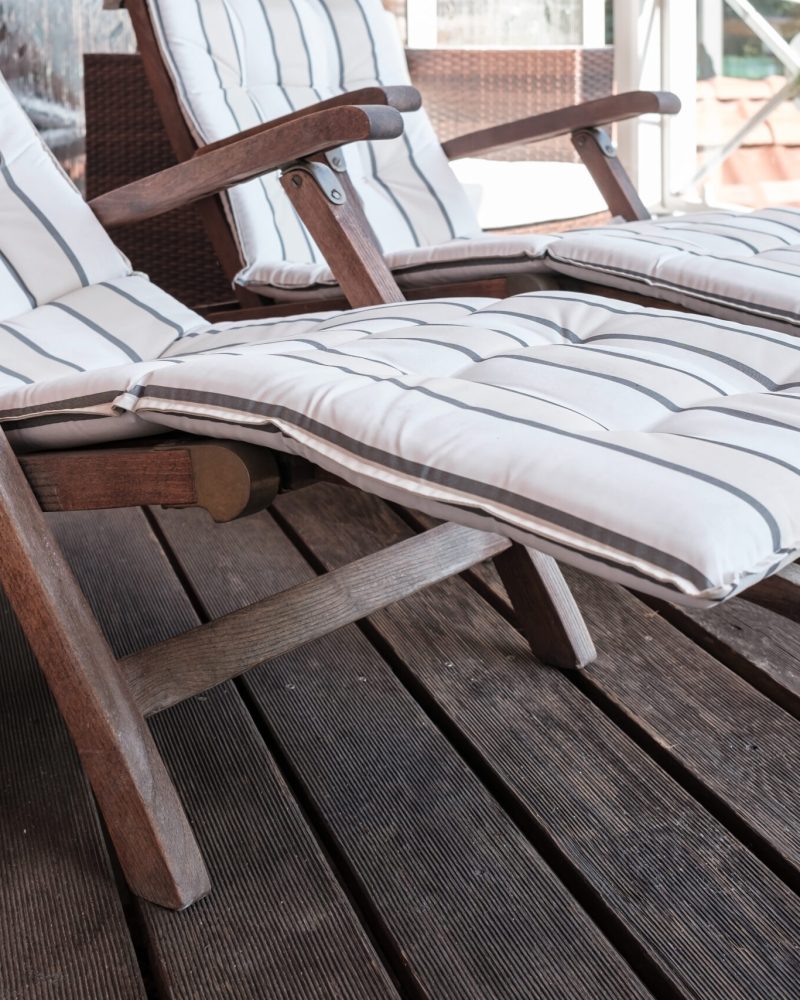 Empty wooden deck chair with a soft pillow on the terrace, against the background of the roofs. Close-up.
